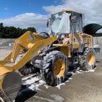 Photo of a yellow loader, halfway through being washed. It is covered in suds