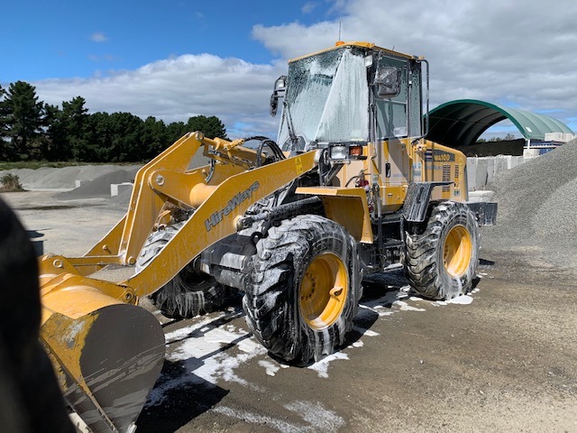 Photo of a yellow loader, halfway through being washed. It is covered in suds