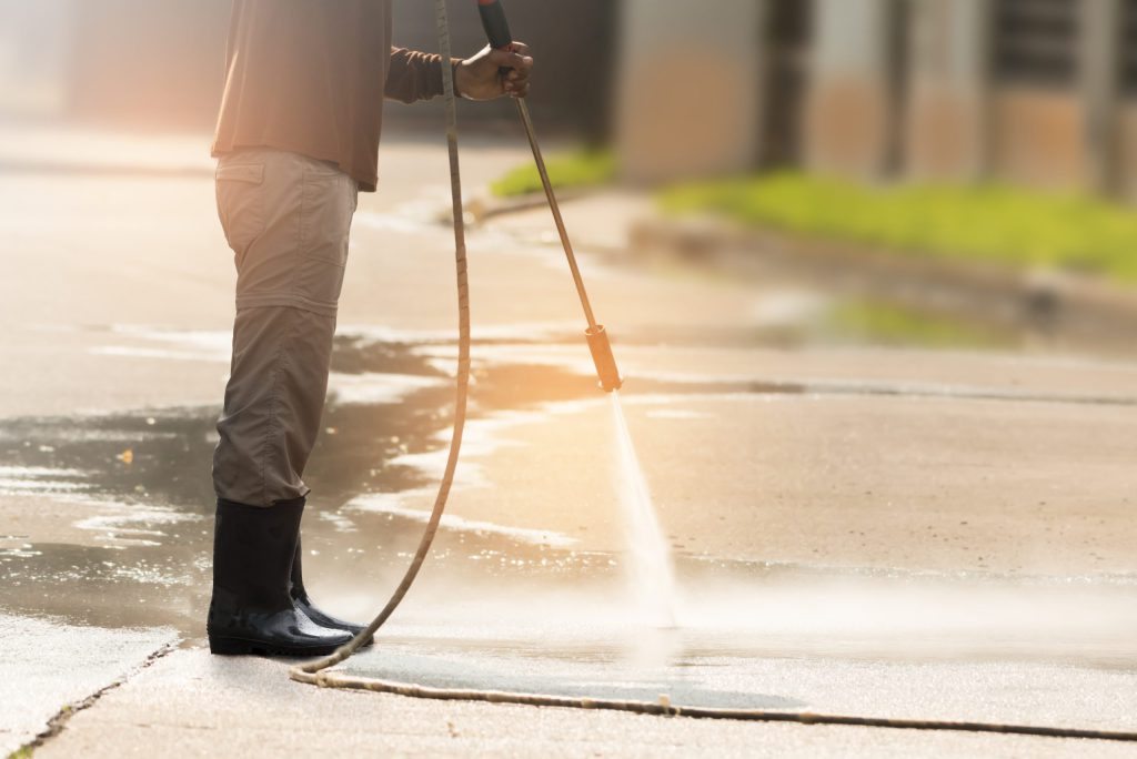 Man standing with waterblaster. He is waterblasting the concrete that he is standing on.